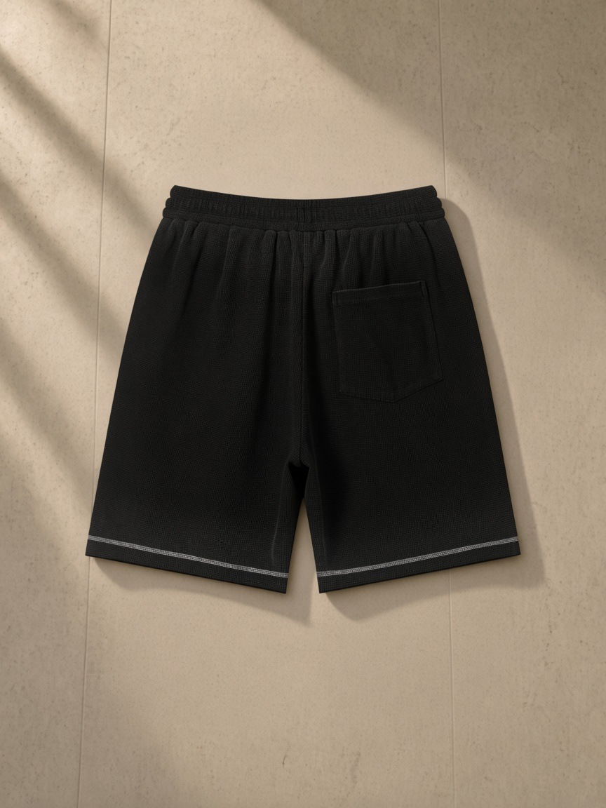 Sunfade Waffle Raw Hem Shorts in Black, laid flat on pale limestone, back.