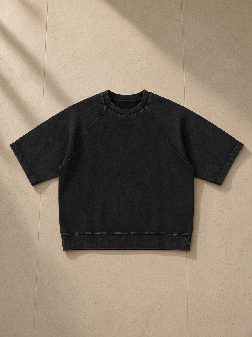 Unisex vintage wash boxy short sleeve sweatshirt in Black, laid flat on pale limestone