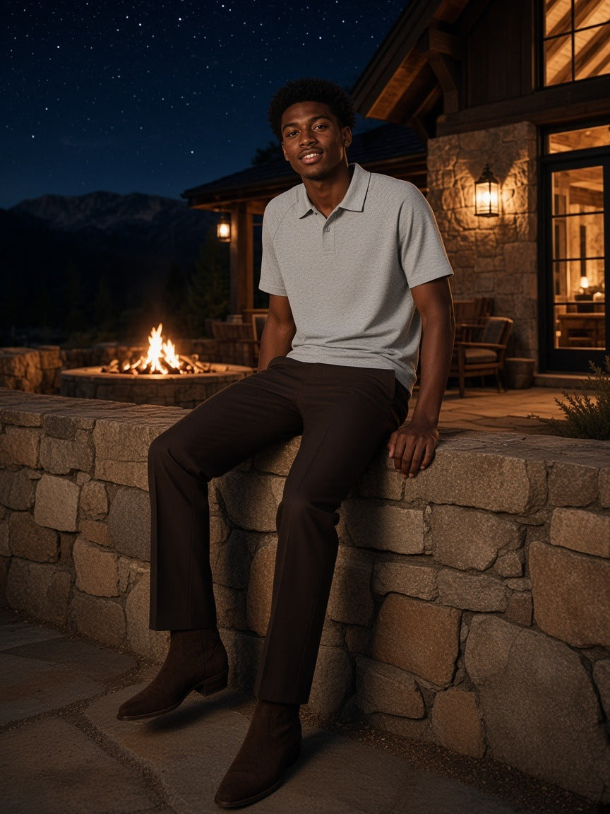 Man in the Classic Knit Polo in Flower Gray, seated on a stone wall at a ranch lodge in Montana at night