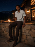 Man in the Classic Knit Polo in Flower Gray, seated on a stone wall at a ranch lodge in Montana at night