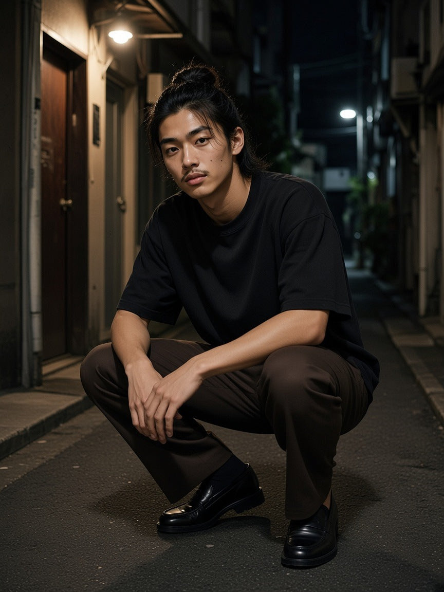 Man in the Classic Loose Boxy Tee in Black crouched in a Golden Gai alley in Tokyo at night