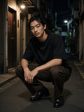 Man in the Classic Loose Boxy Tee in Black crouched in a Golden Gai alley in Tokyo at night
