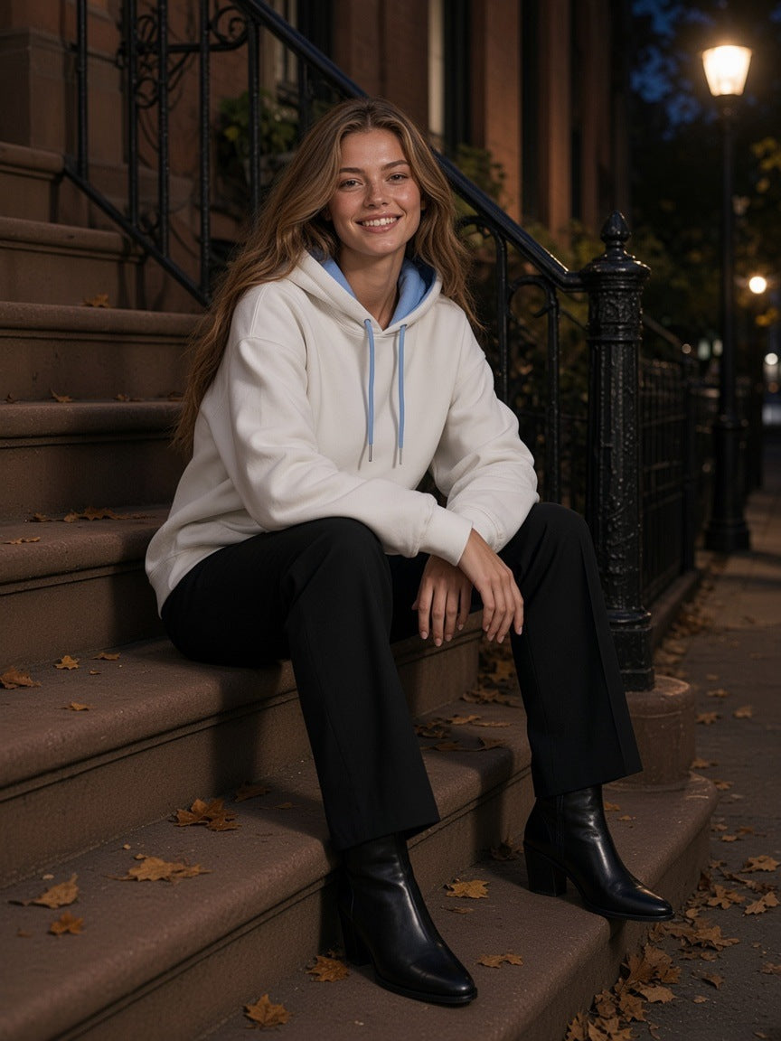 Woman in the Contrast Drawstring Hoodie in White with black trousers and ankle boots, seated on a Brooklyn brownstone stoop at night