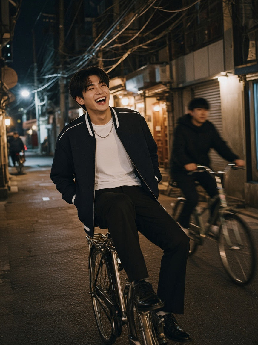 Man in the Marcel Afters Contrast Piping Zip Bomber Jacket in Black walking a hotel corridor above Tokyo at night