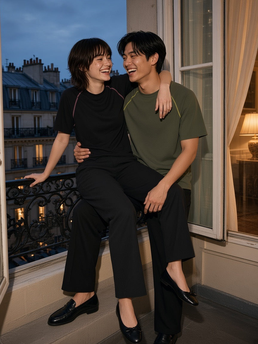 Marcel Afters Contrast Stitch Raglan T-Shirt in Black, worn by a man and a woman, sharing a Paris balcony seat, she in black and he in olive contrast-stitch raglan tees