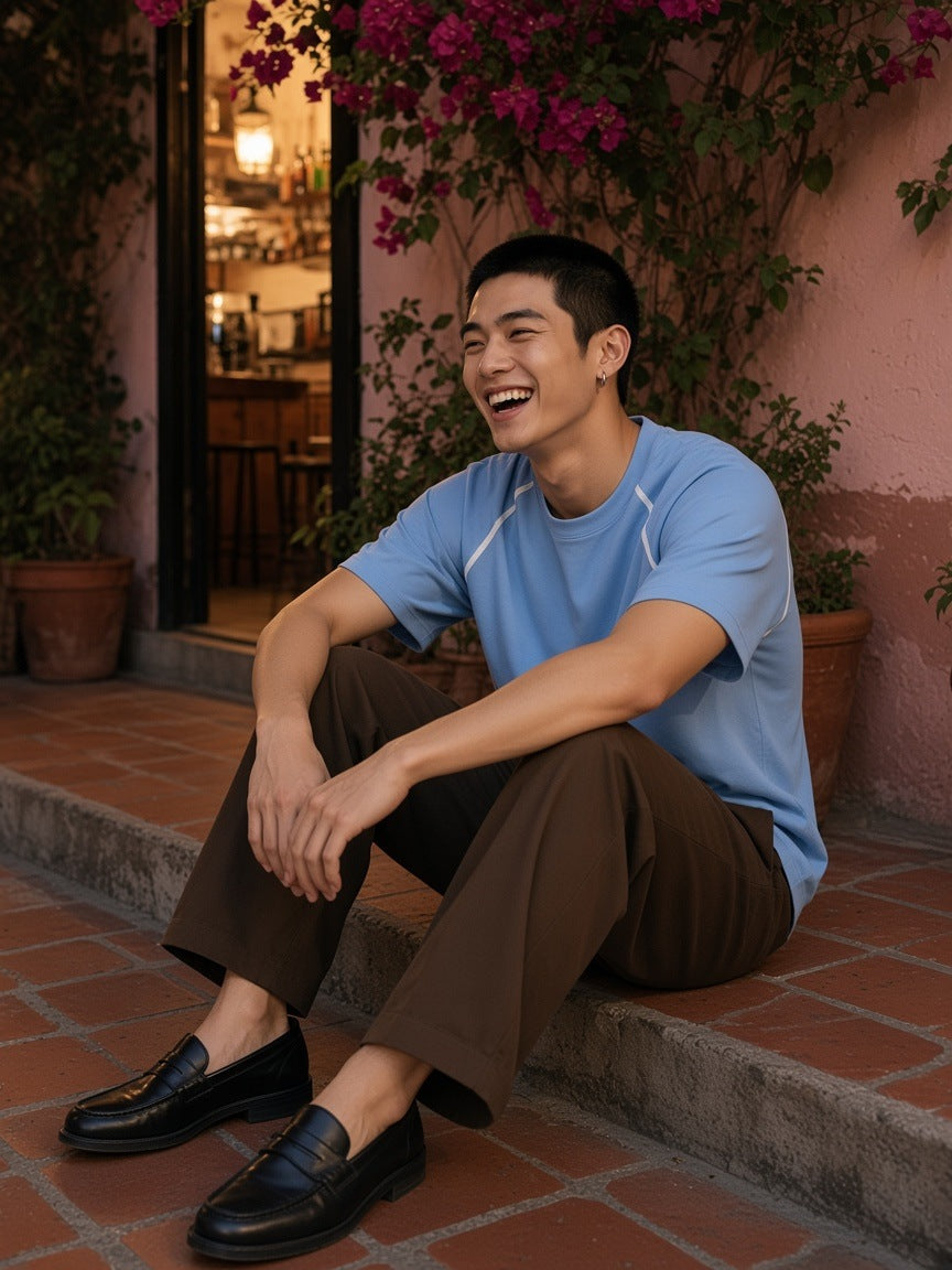 Marcel Afters Contrast Stitch Raglan T-Shirt in Sky Blue, worn by a man, laughing on terracotta steps under bougainvillea in a sky-blue contrast-stitch raglan tee