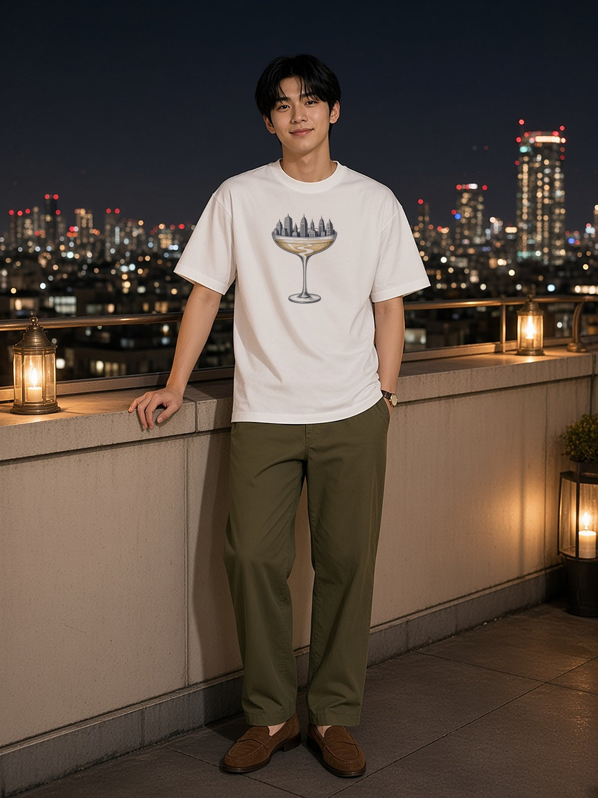 Man in the Coupe Over The City tee in White on a hotel rooftop terrace above the city at night