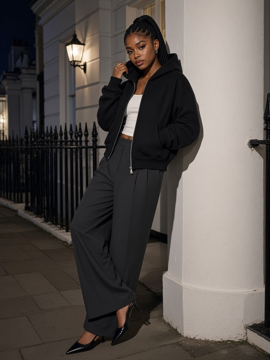 Woman in the Cropped Zip-Through Hoodie in Black over a white tank with wide charcoal wool trousers and pointed slingbacks, leaning on a stucco column on a Belgravia terrace, London at midnight