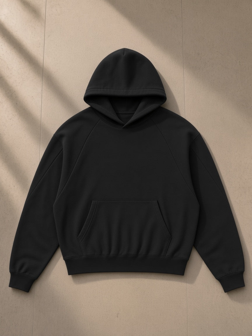 Curved panel raglan hoodie in Black, laid flat on pale limestone, front view