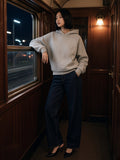 Woman in the Curved Panel Raglan Hoodie in Flower Gray with indigo wide jeans and black slingbacks, at the window of a night-train corridor