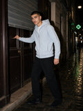 Man in the Raglan Full Zip Hoodie in Light Blue over a white tee with black pleated trousers and suede Chelsea boots, pushing open a bar door on Rue Saint-Denis, Paris at 2am