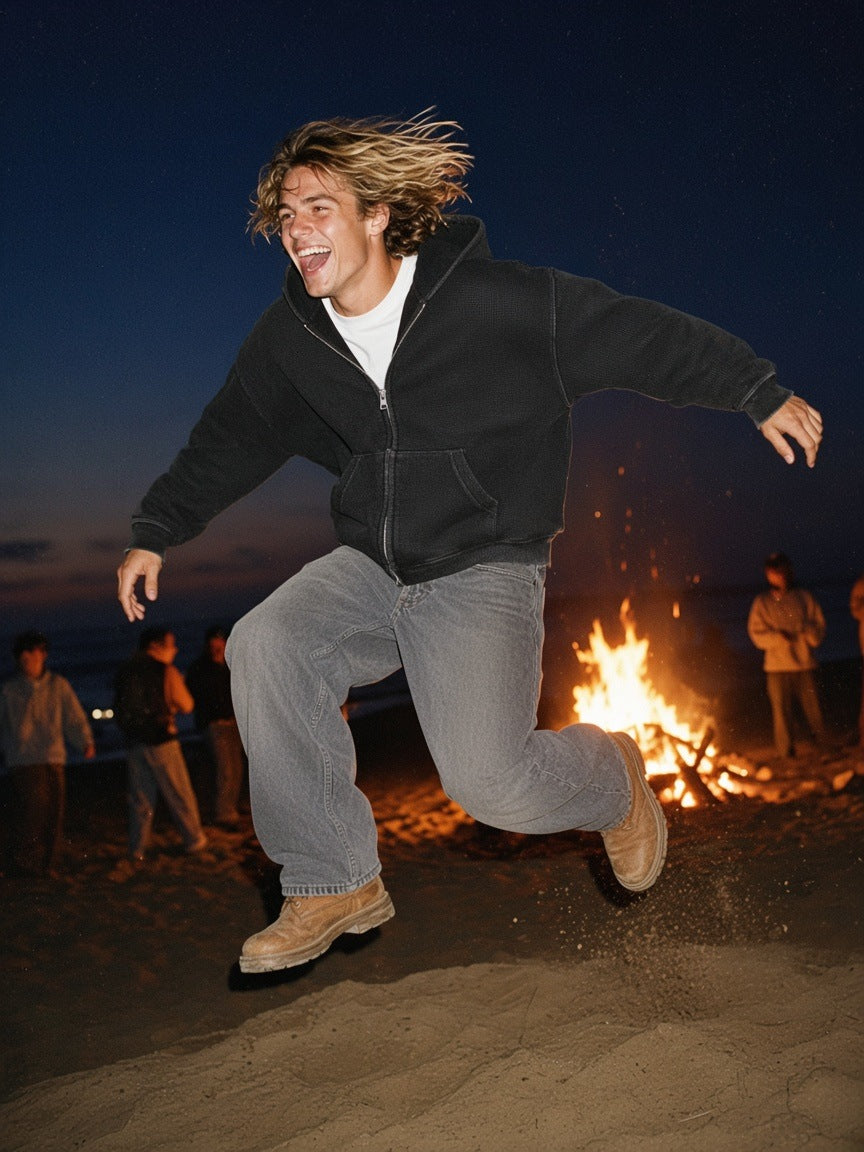 Man in the Vintage Wash Boxy Waffle Full Zip Hoodie in Black, leaping toward a Biarritz beach bonfire at 3am