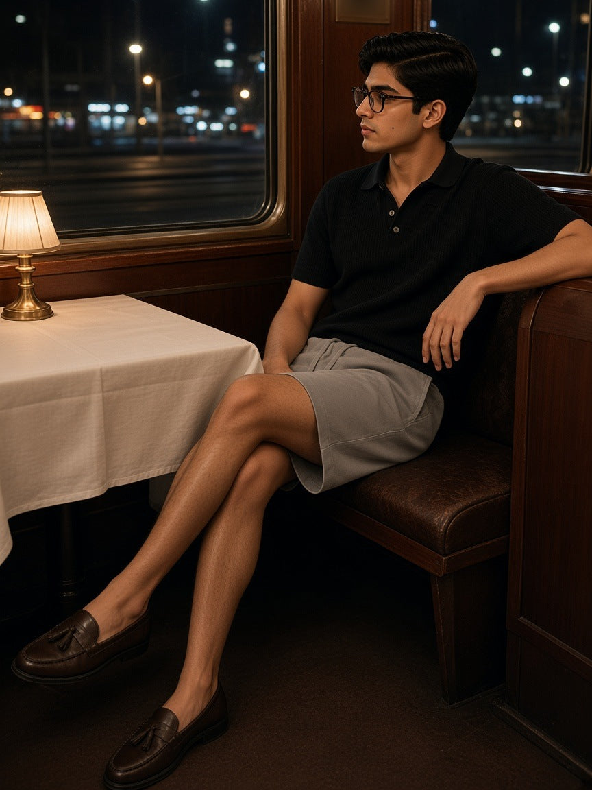 Man in the Vintage Wash Cotton Shorts in Light Coffee with a black knit polo and tassel loafers, seated in a night-train dining car at midnight