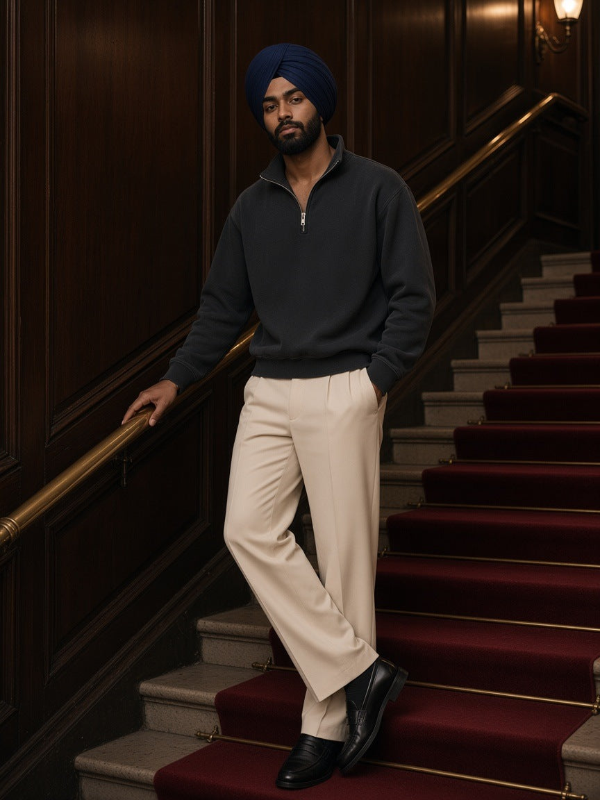 Man in the Vintage Wash Fleece Quarter Zip Sweatshirt in Black with ecru pleated trousers, on a red-carpeted hotel staircase at night