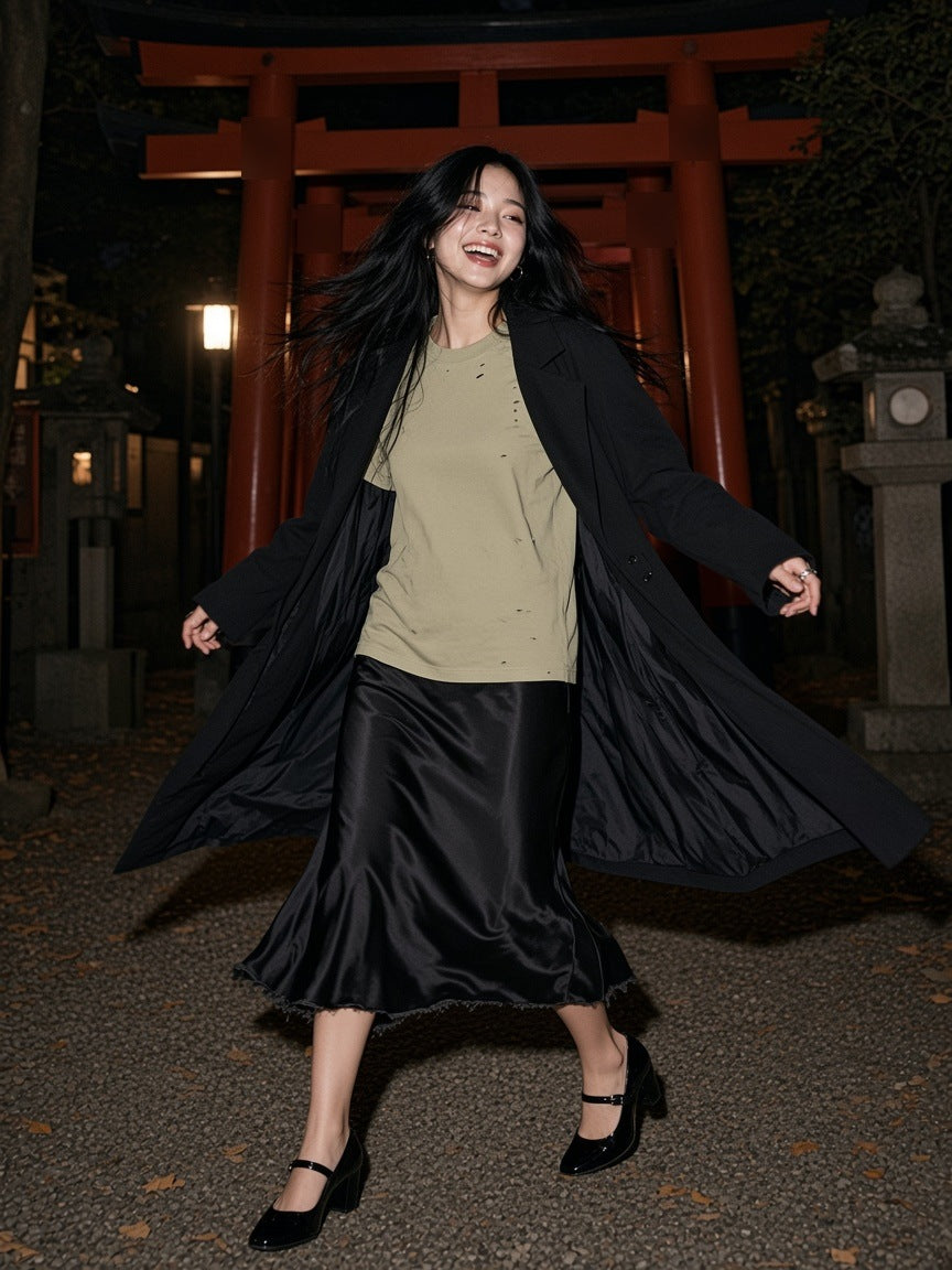 Woman in the Vintage Washed Distressed Boxy Oversized T-Shirt in Pale Khaki with a black satin skirt and long coat, twirling at a Tokyo shrine gate at night