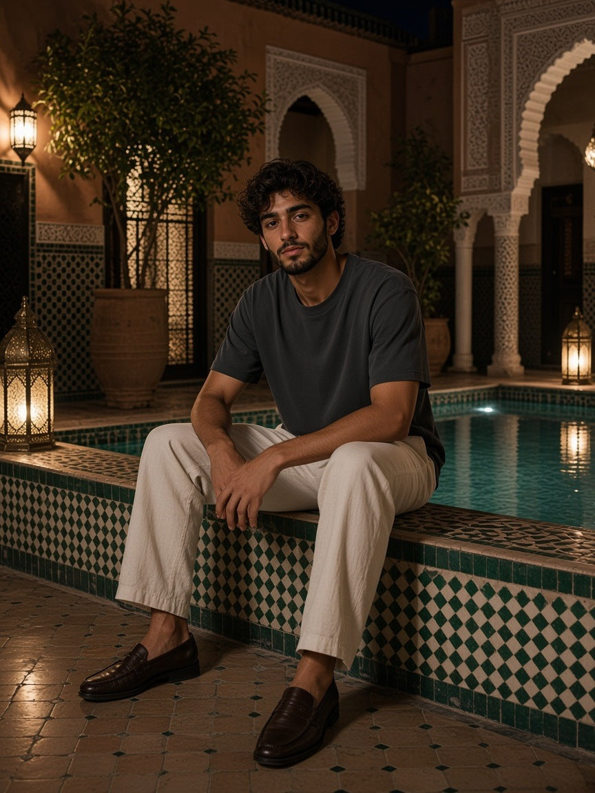 Man in the Marcel Afters Washed Rolled Hem Half Sleeve T-Shirt in Dark Gray, beside a riad hotel pool at night in Marrakech