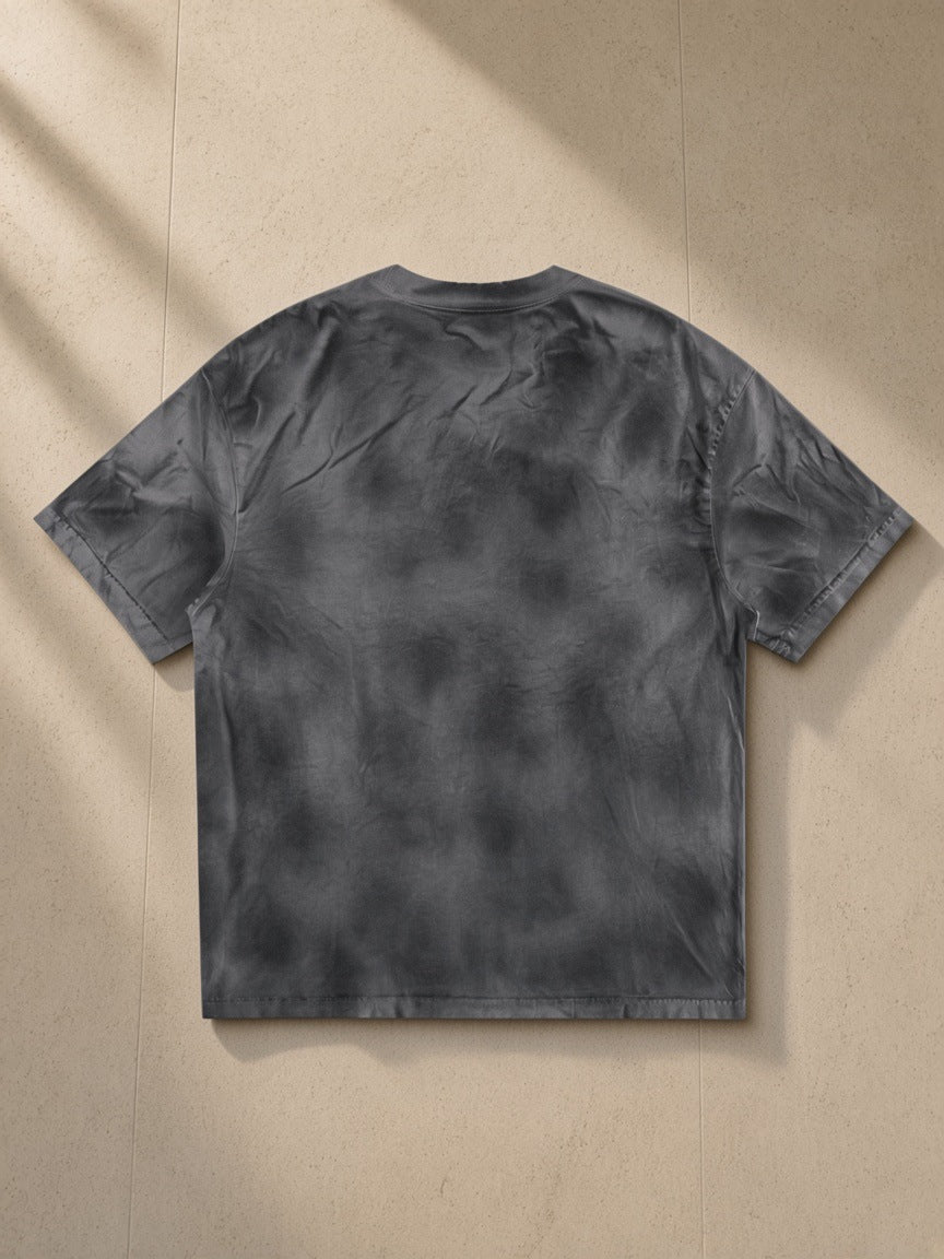 Dirty Washed Loose T-Shirt in Washed Charcoal, laid flat on pale limestone, back view