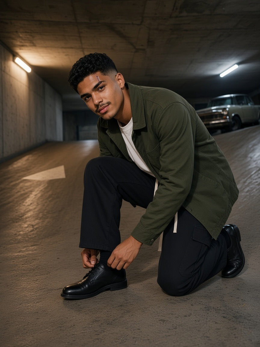 Man in the Drawstring Waist Straight-Leg Cargo Pants in Black with a white tee, olive chore coat and derbies, tying a shoe on a Berlin car park ramp at night