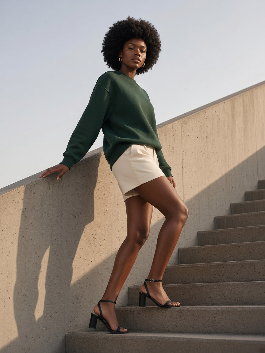 Woman in the Drop Shoulder Crewneck Sweatshirt in Retro Green with cream shorts, climbing a concrete stair in Lagos by day