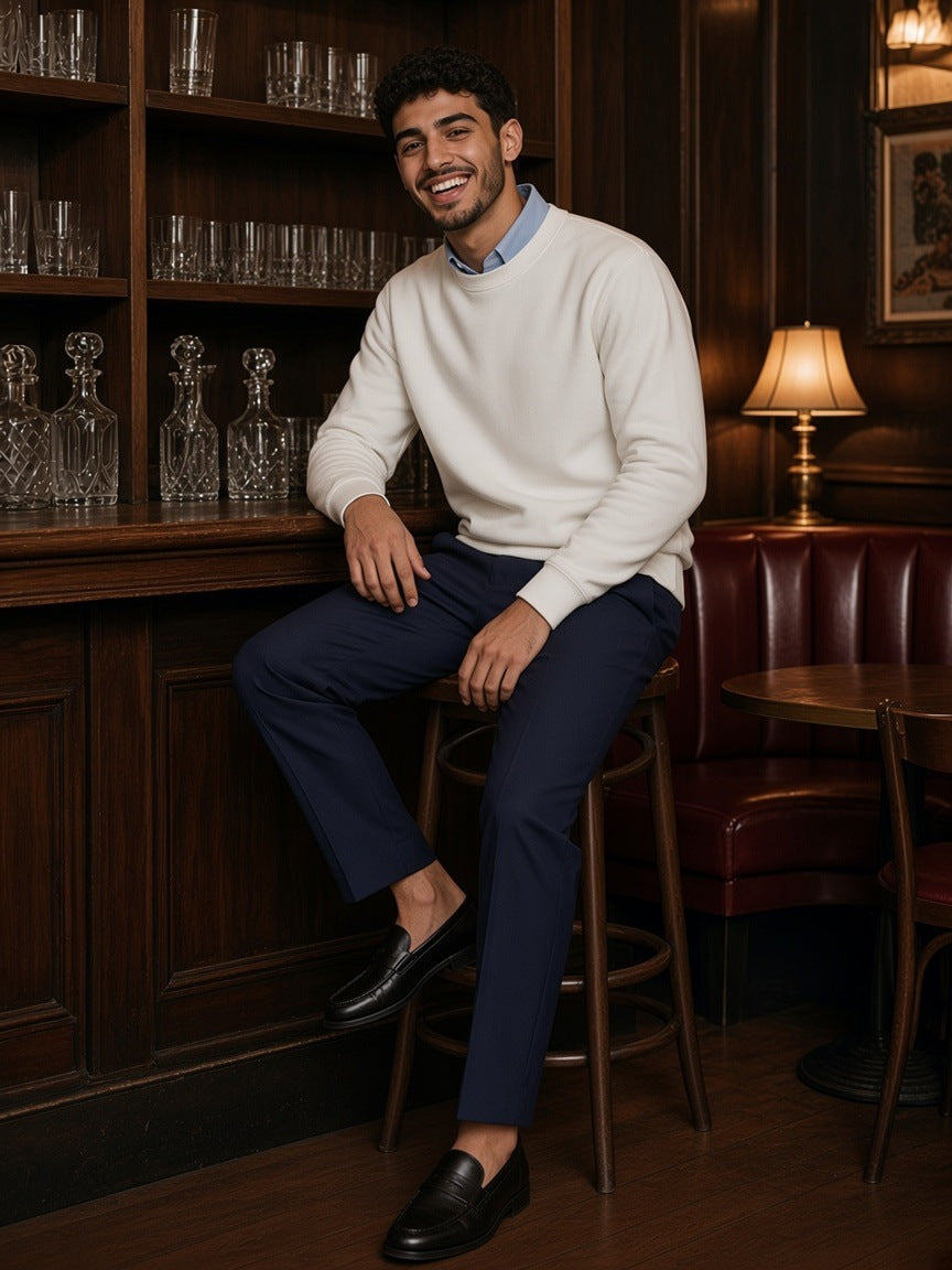 Man in the Drop Shoulder Crewneck Sweatshirt in White over a blue oxford shirt, laughing on a stool at a jazz club bar