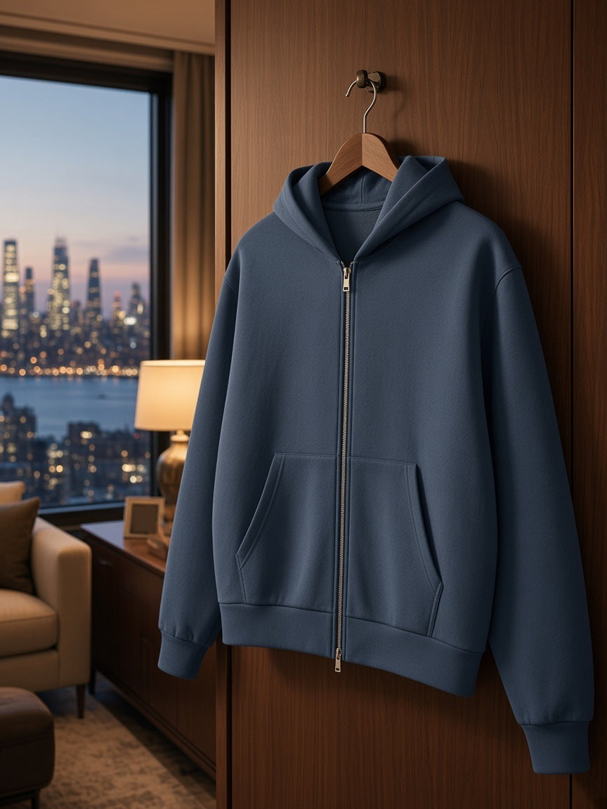 Men's Drop Shoulder Full Zip Hoodie in Slate Blue on a wooden hanger hooked on a walnut wardrobe door in a Hudson rooftop suite at night