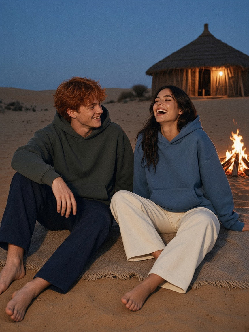 Two people in the Marcel Afters Drop Shoulder Hoodie in Dark Gray and Haze Blue by a dune bonfire at blue hour