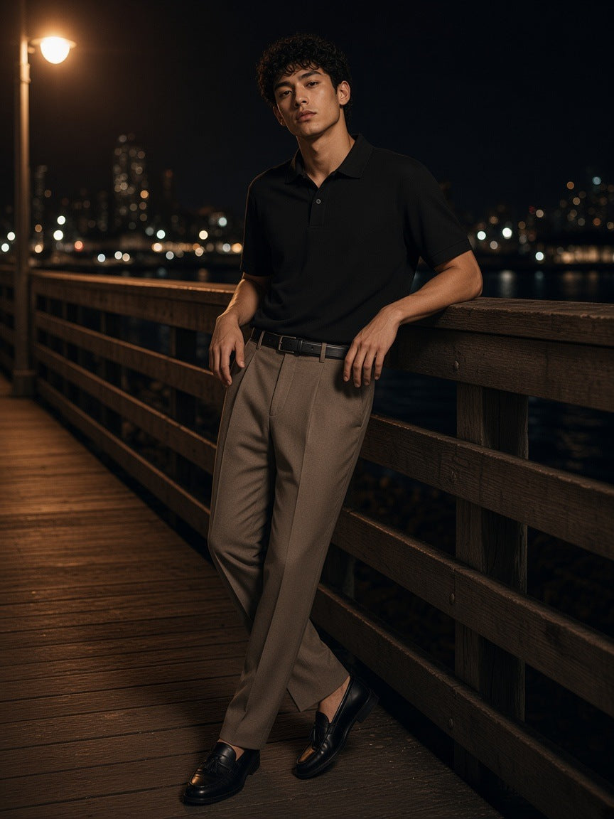 Man in the Drop Shoulder Short-Sleeve Polo in Black leaning on a pier rail in Brooklyn at night