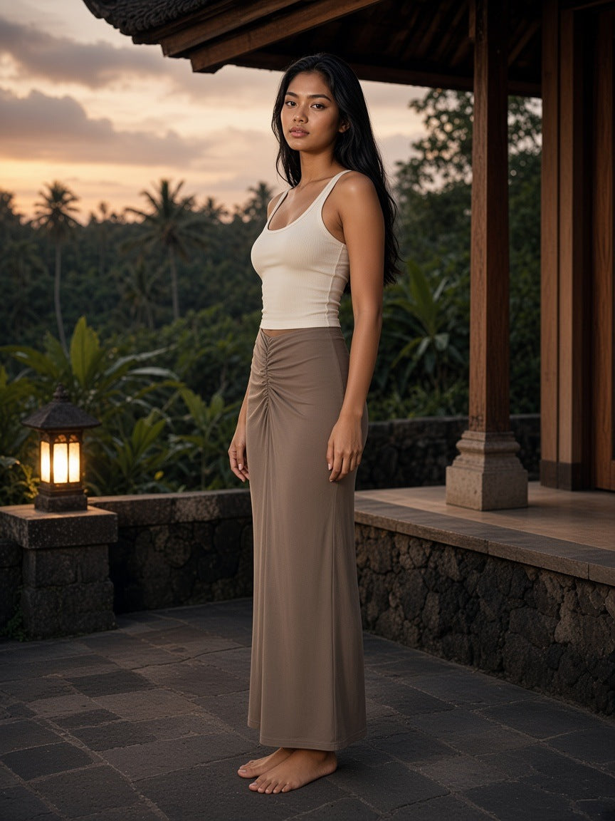Woman in the Marcel Afters Dyed Washed Drawstring Maxi Skirt in Coffee on a volcanic stone resort terrace in Bali at dusk