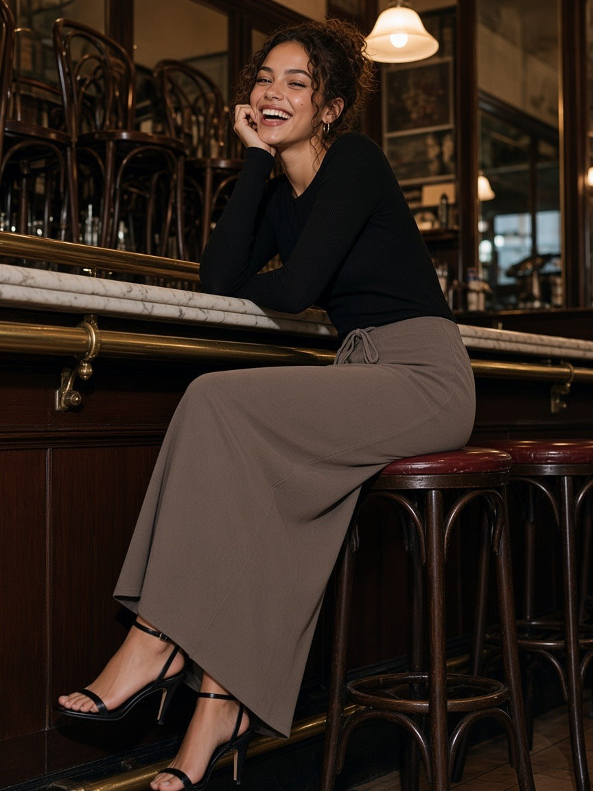 Woman in the Dyed Washed Drawstring Maxi Skirt in Coffee with a black knit and strappy sandals, laughing at the bar of a Vienna café at closing time