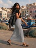 Woman in the Dyed Washed Drawstring Maxi Skirt in Medium Gray with a black cropped tee, leather jacket over her shoulders and strappy sandals, turning on the quay at Procida harbour at golden hour