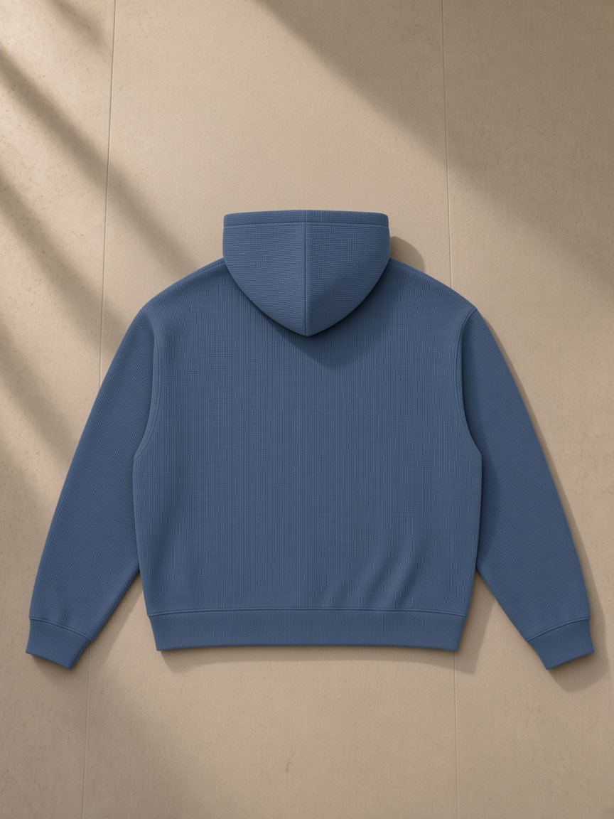 Waffle boxy hoodie in Jeans Blue, laid flat on pale limestone, back view