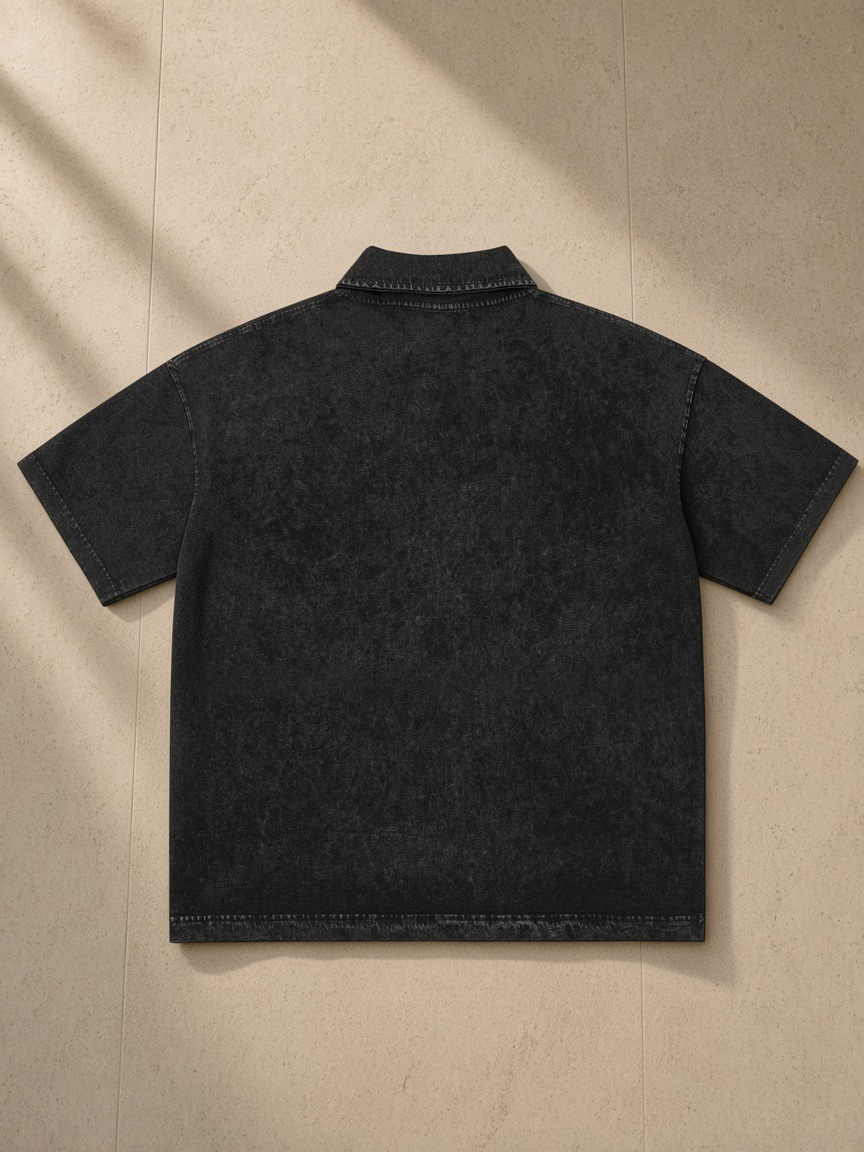 Heavyweight Snow-Washed Polo in Black, laid flat on pale limestone, back view