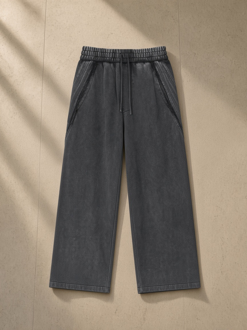Snow Washed Tape Raw Edge Sweatpants in Black, laid flat on pale limestone, front.