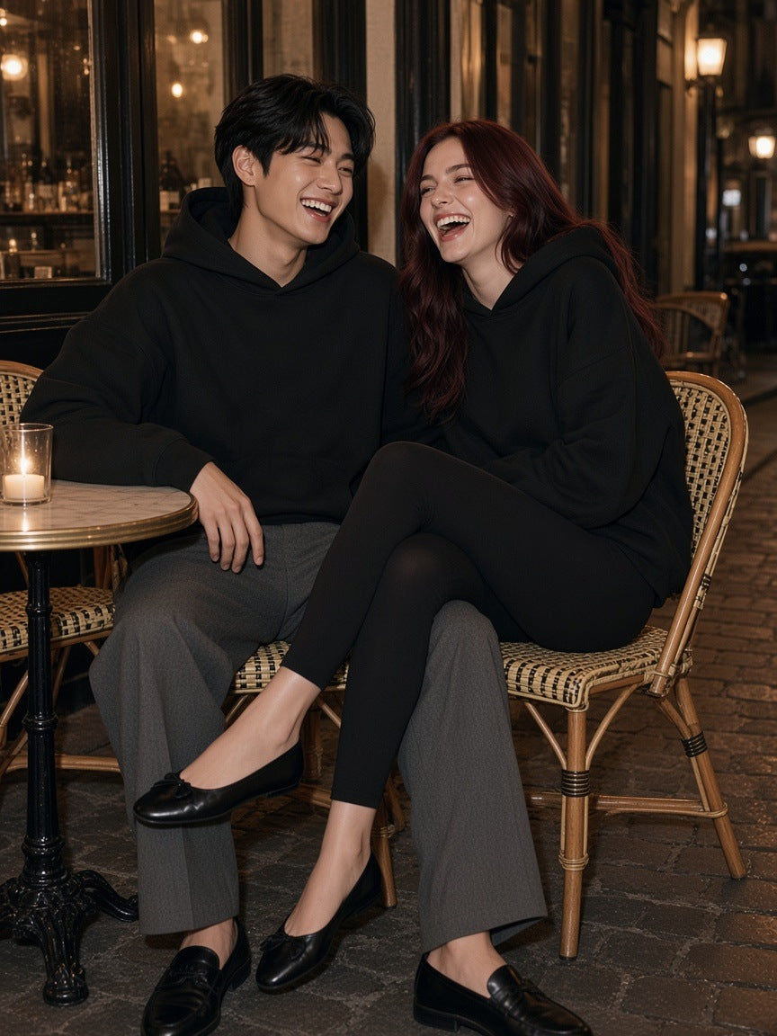 Two people in the Marcel Afters Essential Boxy Darted Sleeve Hoodie in Black at a Paris cafe table at night