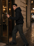 Man in the Essential Boxy Heavyweight Drop-Shoulder Hoodie in Black pushing open a hotel bar door in Paris at night