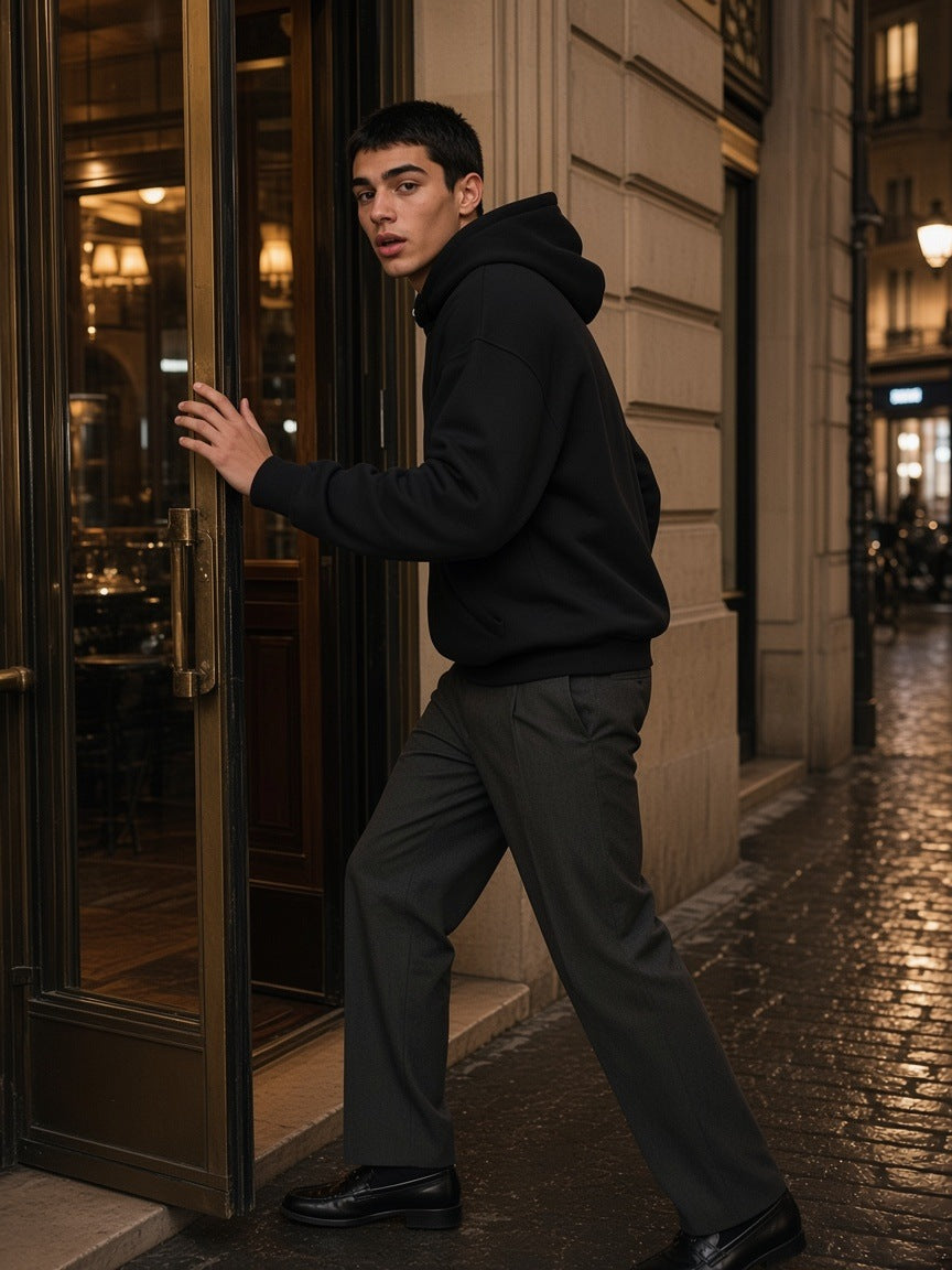 Man in the Marcel Afters Essential Boxy Heavyweight Drop-Shoulder Hoodie in Black pushing open a hotel bar door in Paris at night