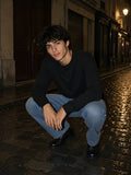 Man in the Essential Cotton Long Sleeve T-Shirt in Black squatting on wet Paris cobbles at night