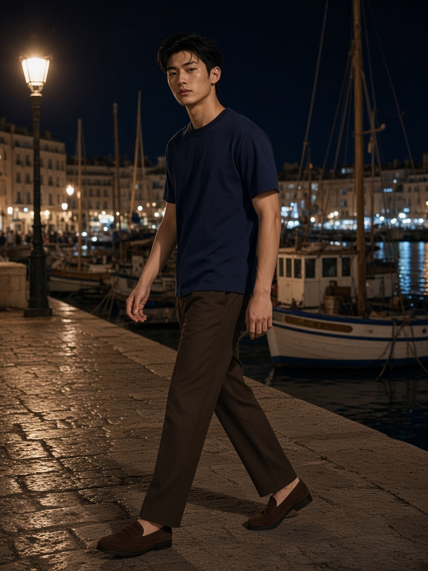 Marcel Afters Essential Cotton T-Shirt in Navy Blue, worn by a man, walking a lamp-lit harbour quay at night in a navy tee and dark trousers