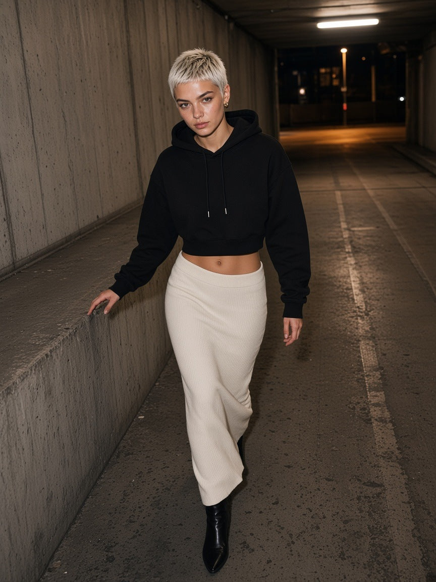 Woman in the Essential Cropped Hoodie in Black with an ivory knit maxi skirt, walking up a car park ramp in Berlin at night