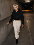 Woman in the Essential Cropped Hoodie in Black with an ivory knit maxi skirt, walking up a car park ramp in Berlin at night