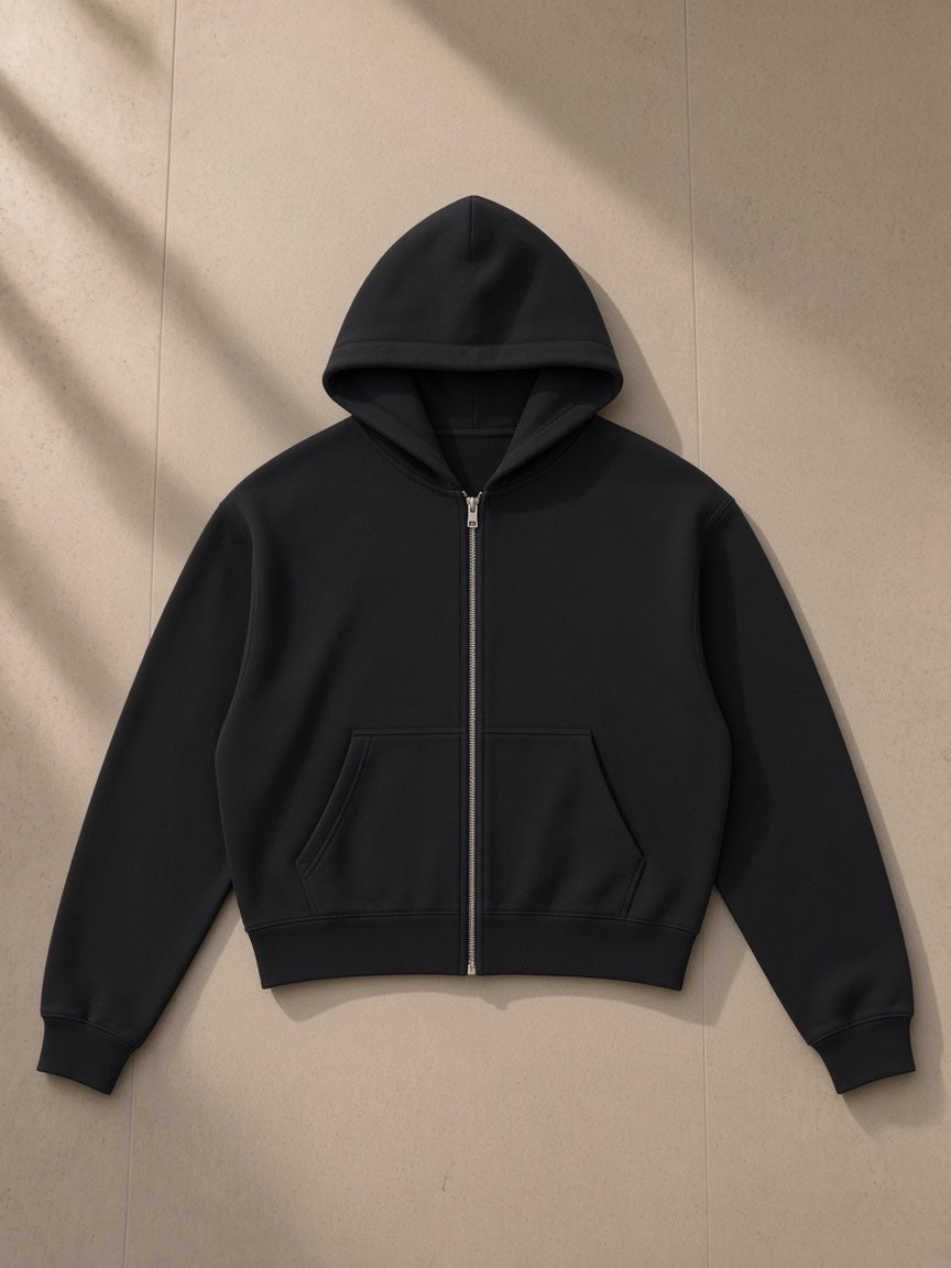 Essential cropped zip-up hoodie in Black, laid flat on pale limestone, front view
