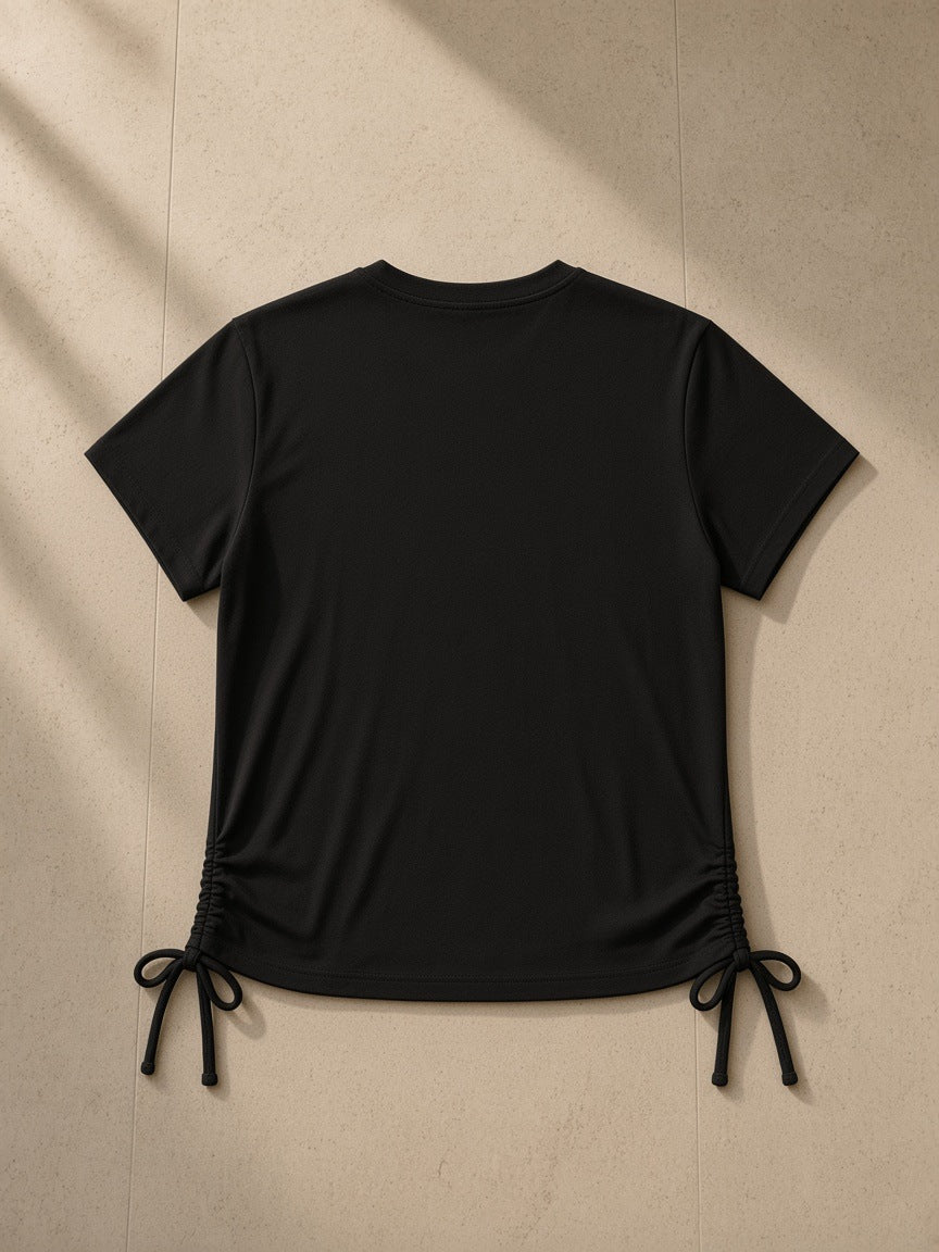 Essential Drawstring T-Shirt in Black, laid flat on pale limestone, back view
