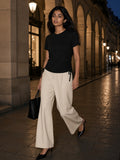 Woman in the Essential Drawstring T-Shirt in Black with ecru wide-leg trousers and black slingbacks, walking through the Rue de Rivoli arcade in Paris at night