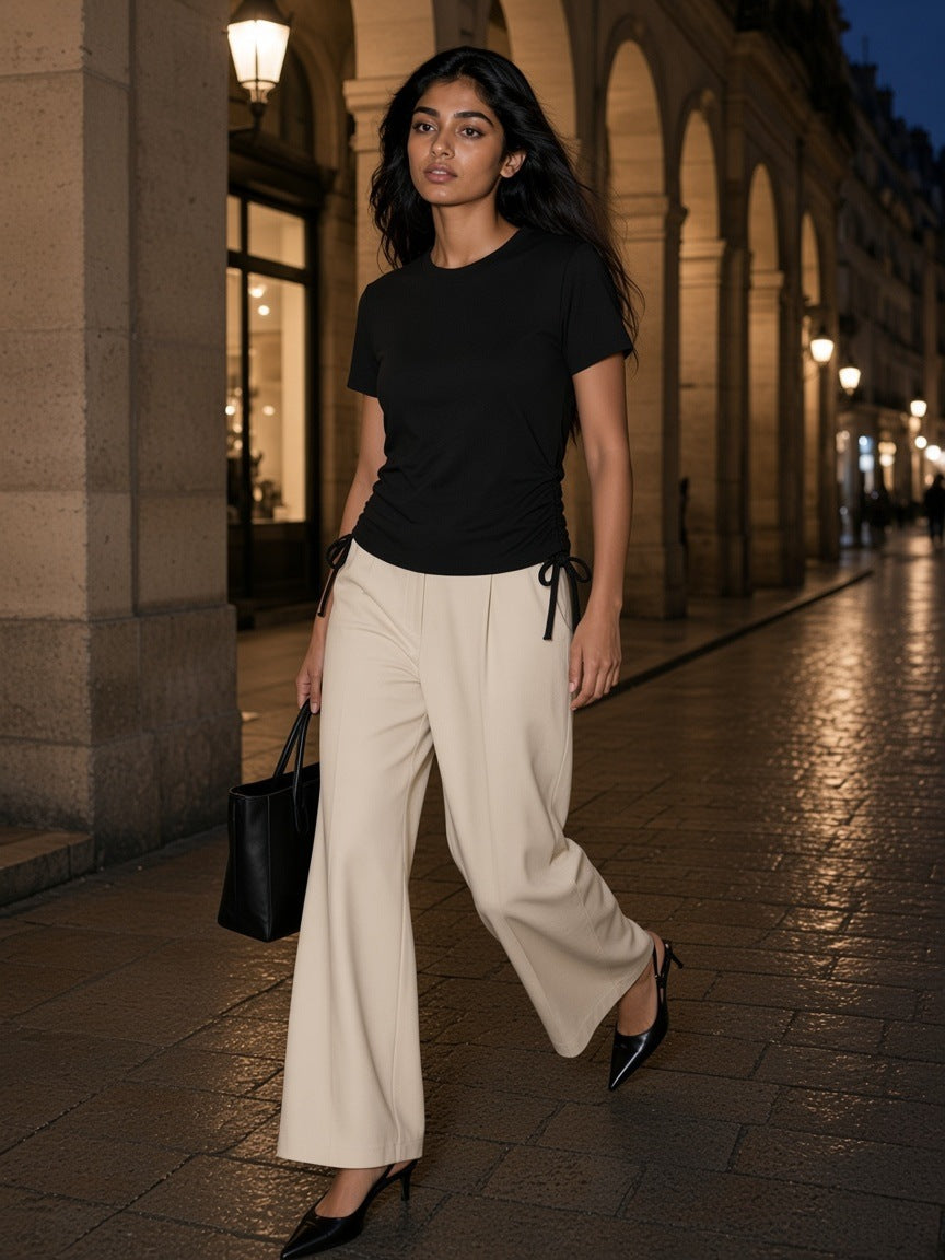 Woman in the Essential Drawstring T-Shirt in Black with ecru wide-leg trousers and black slingbacks, walking through the Rue de Rivoli arcade in Paris at night