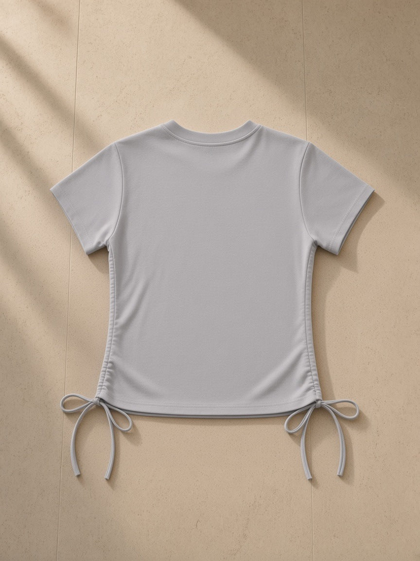 Essential Drawstring T-Shirt in Light Gray, laid flat on pale limestone, back view