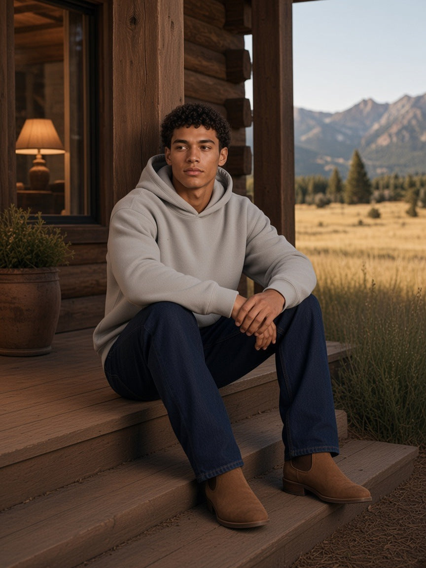 Man in the Essential Heavyweight Boxy Fleece Hoodie in Oat Gray sitting on the porch steps of a ranch lodge in Montana in the morning