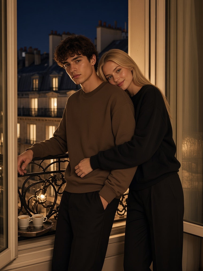Marcel Afters Essential Heavyweight Crewneck Sweatshirt — Dark in Coffee, worn by a man and a woman, embracing on a Paris balcony at night, he in a coffee sweatshirt and she in black