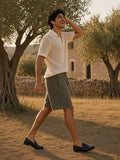 Man in the Essential Heavyweight Fleece Shorts in Olive Green with an ecru open-knit polo and black penny loafers, walking laughing through the olive trees of a Mallorca finca at golden hour
