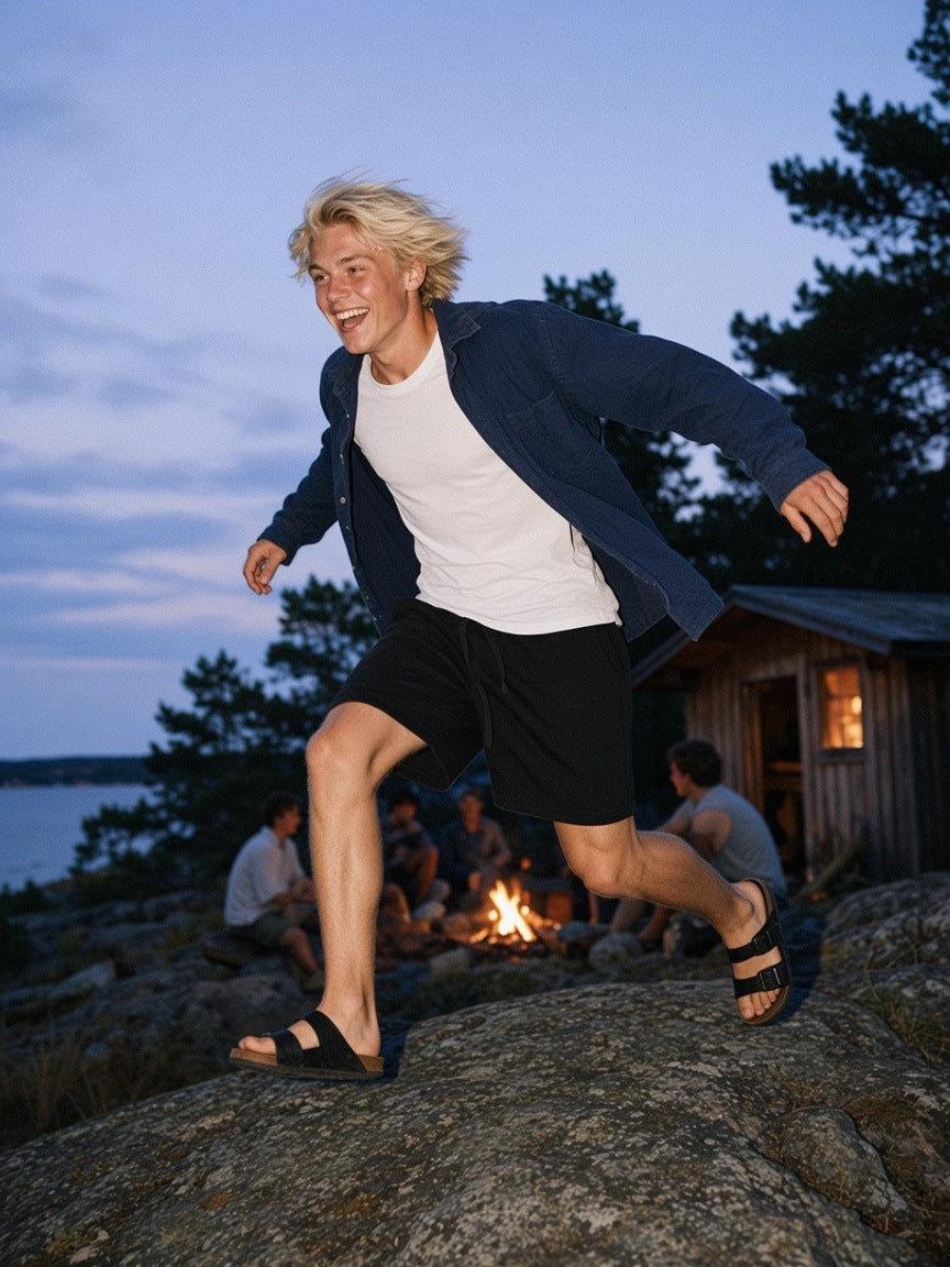 Man in the Essential Heavyweight Fleece Shorts in Black, leaping across granite by a midnight bonfire in the Stockholm archipelago