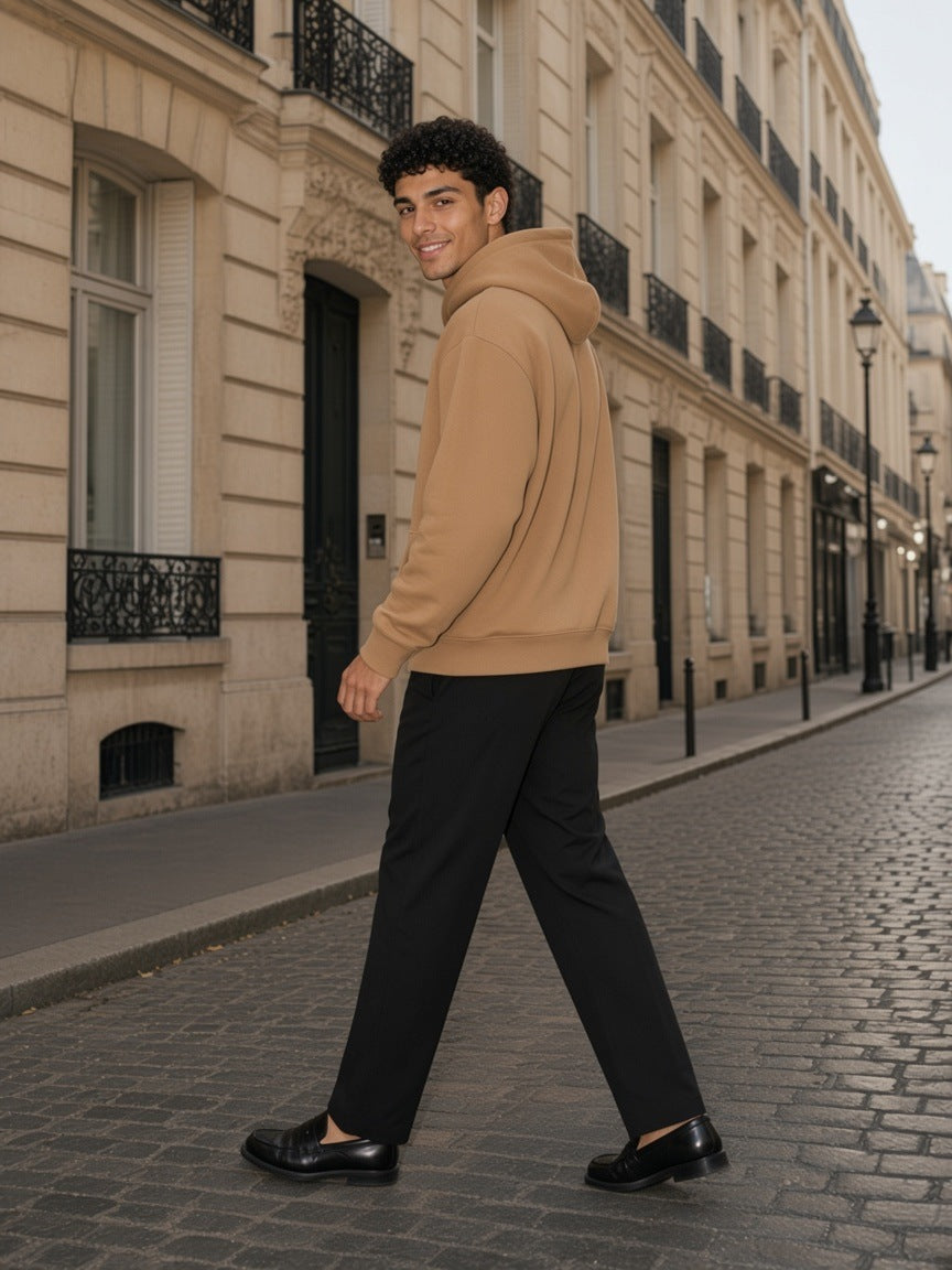 Man in the Essential Heavyweight Hoodie, 400 gsm in Camel walking down a Haussmann street in Paris in the morning